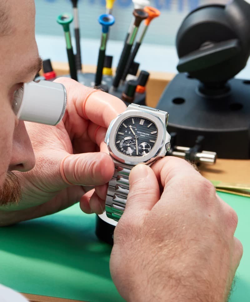A watchmaker inspecting a watch through a loupe